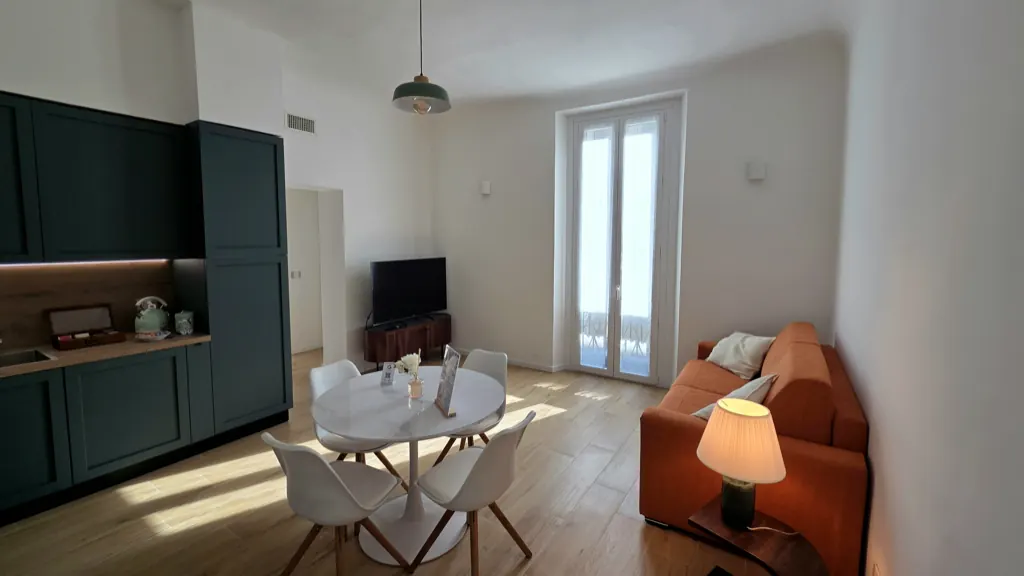 Soggiorno aperto sulla cucina, con TV e portafinestra luminosa